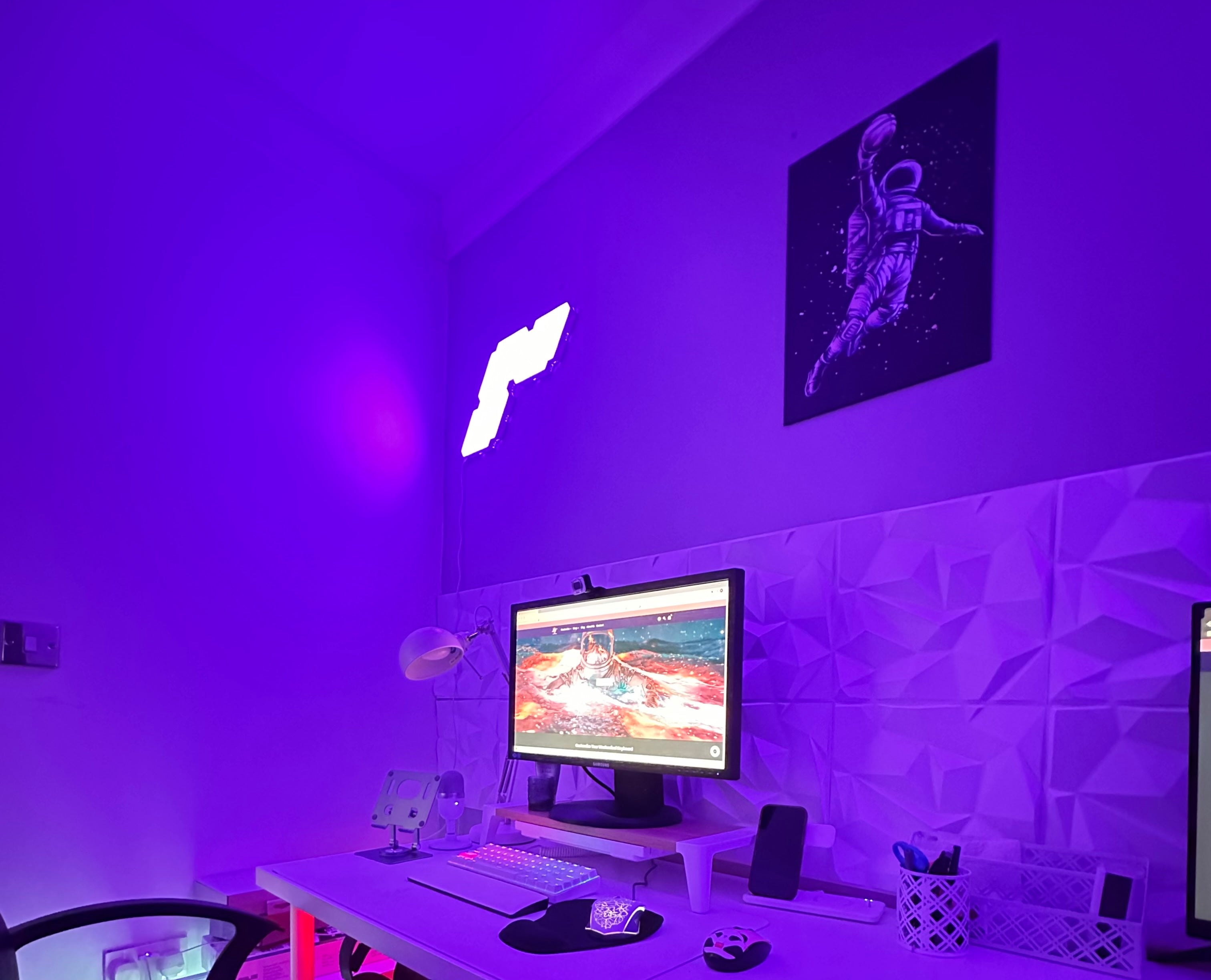 purple gaming room with 3d white panel as decor with astronaut frame on the wall and two monitors 